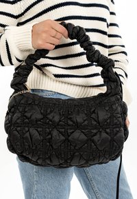 Black quilted handbag with a gathered handle, featuring a textured pattern and a gold chain accent. The fabric appears soft and padded.