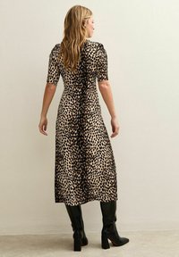 Vestido midi de estampado de leopardo en beige y negro, con mangas cortas, un cuerpo ajustado y una falda acampanada. Combinado con botas negras hasta la rodilla.