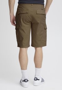 Brune cargo shorts med to sidelommer, flad talje og dobbelte baglommer. Bæret med hvide ankelstrømper og sorte stribede sneakers.