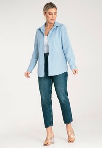 Jasnoniebieska koszula w paski z rozłożystym kołnierzem, połączona z ciemnoniebieskimi spodniami z wysokim stanem i przezroczystymi sandałami na obcasie.