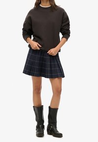 Sudadera gris oscuro con cuello alto, falda plisada azul marino a cuadros y botas negras de cuero hasta la rodilla con hebillas.