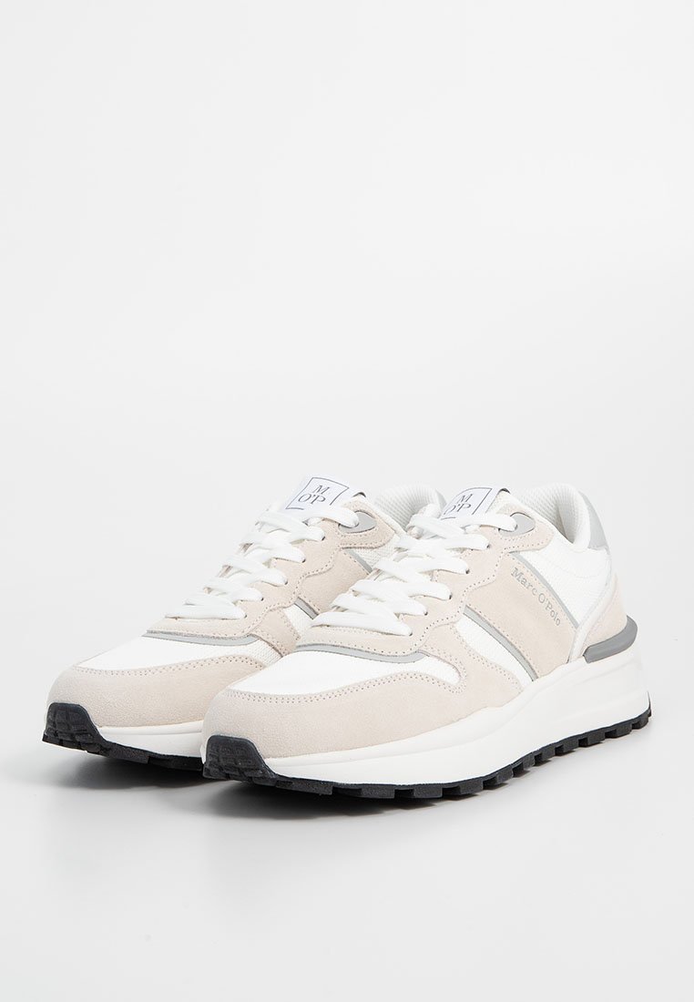 Beige und weiße Sneakers aus Leder und Wildleder mit einem flachen Design, ausgestattet mit Schnürsenkeln, Logo-Akzenten und schwarzen Gummisohlen.