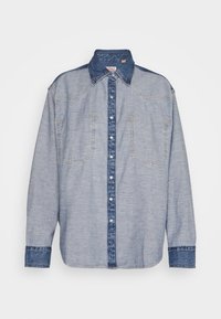 Chemise en denim bleu clair avec un col et des rabats de poche bleu plus foncé, dotée de boutons sur le devant et de manches longues.