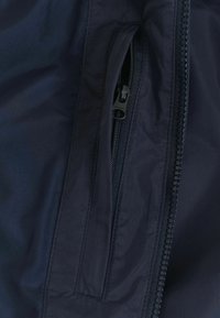 Marineblauwe jasstof met een gladde textuur, voorzien van een zijzak met rits, een zwarte rits met een sportief ontwerp en gestikte naden.