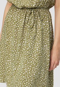 Grön klänning i mjukt tyg med vita prickar, med en sammanknuten midja och justerbar knytning.