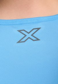 Svetlo modrý atletický top vyrobený zo štruktúrovanej látky, s mriežkovým vzorom a tmavosivým logom "X" blízko výstrihu.