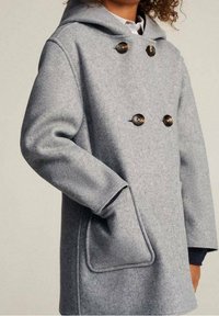 Manteau en laine gris avec une capuche, design à double boutonnage, grands boutons et poches latérales. Texture douce, coupe décontractée et détails de couture minimalistes.