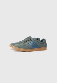 Zapatillas de ante verdes con rayas azules, suelas de goma y superposiciones texturizadas; cuenta con un diseño clásico de cordones y cuellos acolchados.