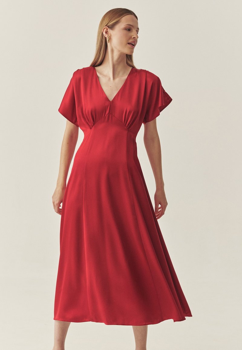 Robe en satin rouge avec un décolleté en V, des manches courtes volantes, et une silhouette fluide en ligne A, présentant une texture lisse et une couleur unie.