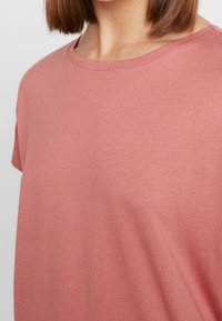 Camiseta de algodón rosa con cuello redondo, mangas cortas y una textura suave y lisa. Presenta un corte relajado y detalles de costura mínimos.
