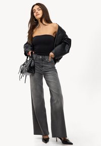 Femme portant un haut tube noir, une veste en cuir noir oversized, un jean large taille haute noir décoloré, tenant un sac à main noir et des talons noirs.