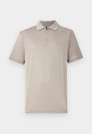 Polo shirt beige chiaro a maniche corte con colletto zip e un piccolo logo sul lato sinistro del petto. Il tessuto sembra liscio e elastico.