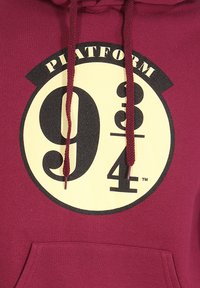 Czerwony hoodie z dużą żółtą grafiką z napisem "Platform 9¾" w kolorze czarnym. Zawiera przednią kieszeń i dopasowane czerwone troczki.