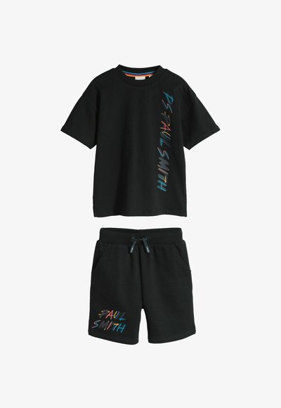 Ensemble t-shirt noir à manches courtes et short avec le texte coloré "PAUL SMITH" imprimé verticalement sur le t-shirt et sur la jambe gauche du short.