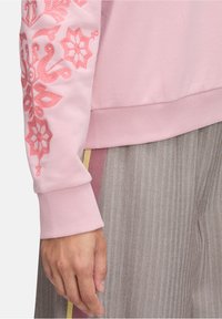 Felpa rosa con ricamo floreale sulla manica, polsini e orlo a costine. Abbinate a pantaloni grigi a spina di pesce con strisce colorate.