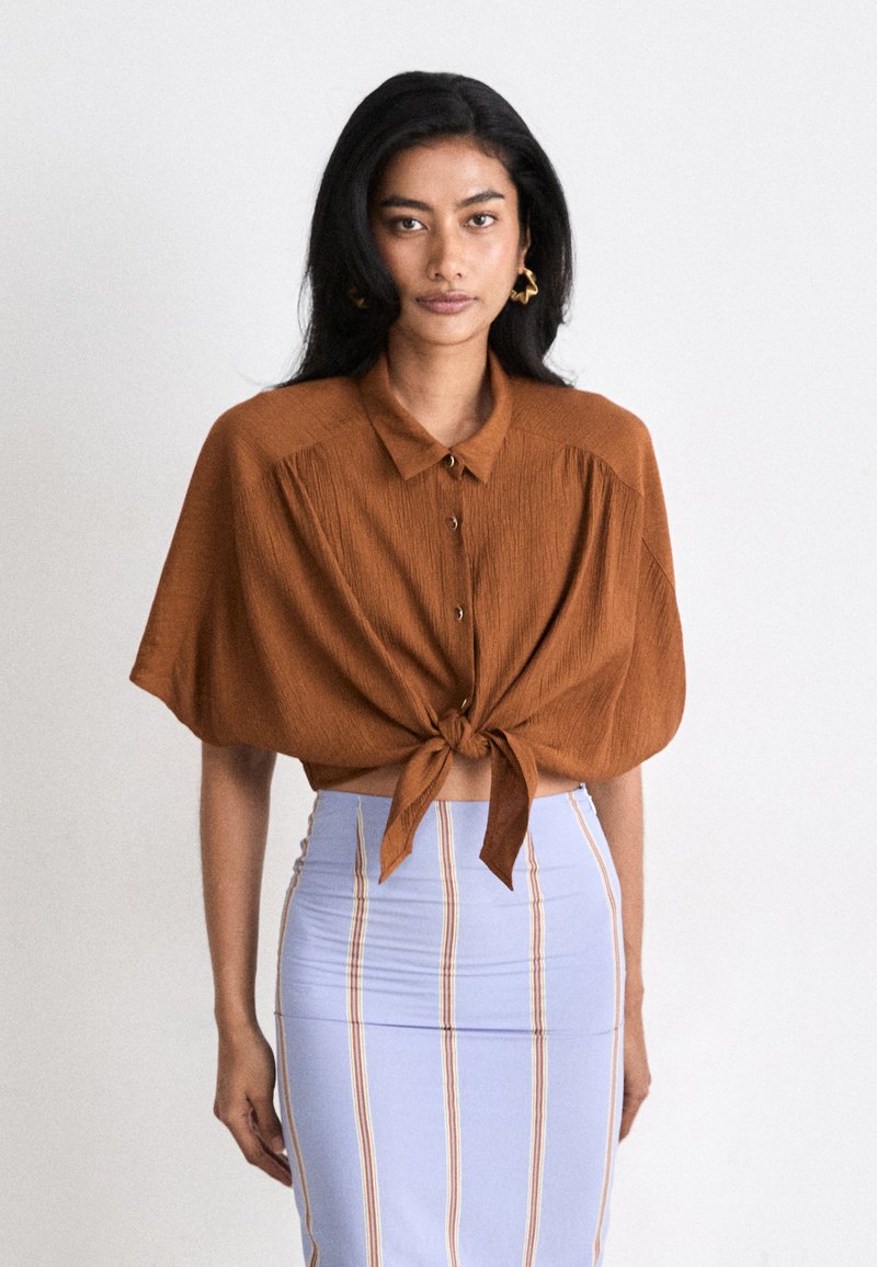 Brown, short-sleeve, button-up shirt with a knotted front, paired with a light blue pencil skirt featuring vertical stripes in various colors.