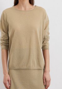 Beige gebreide trui met een ontspannen pasvorm, ronde hals en opgerolde mouwen, gemaakt van zacht materiaal. Gladde tekstuur met een subtiele glans.