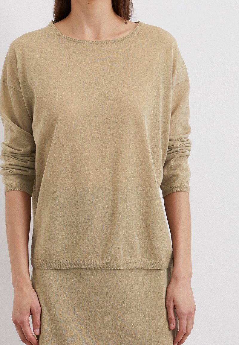 Beige gebreide trui met een ontspannen pasvorm, ronde hals en opgerolde mouwen, gemaakt van zacht materiaal. Gladde tekstuur met een subtiele glans.