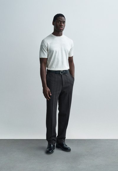 Ανοιχτό γκρι πλεκτό μπλουζάκι με κοντά μανίκια και οριζόντια υφή, σε συνδυασμό με σκούρο παντελόνι με σχέδια και μαύρα παπούτσια. Μινιμαλιστικός σχεδιασμός, εφαρμοστή σιλουέτα.