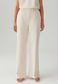 Beige wijde broek van gladde stof met een elastische tailleband. Heeft een strakke uitstraling en subtiele verticale textuurdetails.