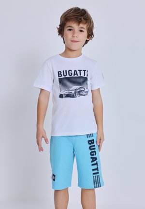 Ragazzo giovane in piedi, indossa una maglietta bianca con una grafica di un'auto e la scritta "BUGATTI" e pantaloncini blu con la scritta "BUGATTI" sul lato.
