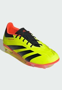 Chaussure de foot jaune vif avec des accents noirs et un intérieur rouge éclatant. Présente une surface texturée et plusieurs crampons pour une meilleure traction.