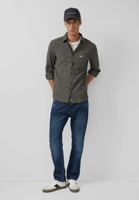 Grijze button-up shirt met opgerolde mouwen, blauwe jeans en witte sneakers met donkere accenten en een donkere baseballcap. Eenvoudig ontwerp.