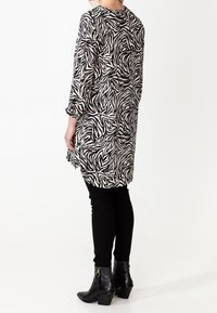 Black and white zebra-striped long tunic with three-quarter sleeves, paired with black fitted pants and ankle boots, featuring a sleek design.