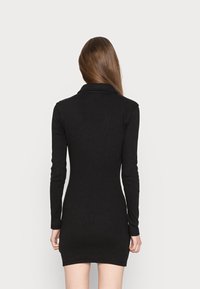 Svart klänning med lång ärm och figurnära silhuett samt krage. Tillverkad av ett strukturerat tyg och når till mitten av låret.