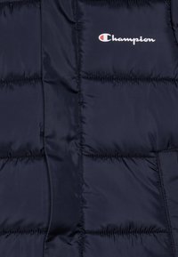 Chaqueta acolchada de color azul marino con diseño acolchado, textura lisa y brillante, y logo blanco de Champion en el lado izquierdo del pecho. Material ligero e insulated.