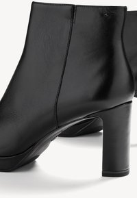 Bottines en cuir noir avec talons blocs, surface lisse et coutures visibles sur les côtés, présentées sur un fond blanc.
