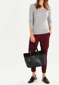 Borsa tote in pelle nera con una texture liscia e una parte superiore in tessuto a contrasto. Presenta una tasca frontale con zip e manici robusti.