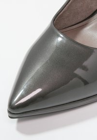 Gros plan d’une chaussure pointue gris foncé brillante avec une surface lisse et réfléchissante et une semelle assortie.