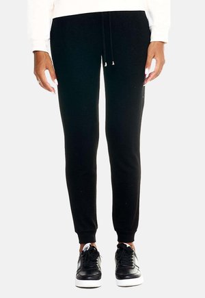 Modèle portant un pantalon de jogging noir fuselé avec un cordon de serrage à la taille et des baskets noires à semelles blanches.