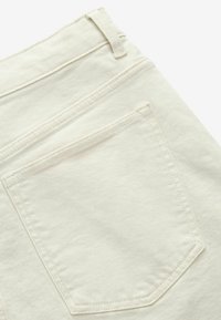 Tissu en denim blanc avec une poche arrière visible, présentant des coutures discrètes et une texture lisse. La poche a un design courbé.