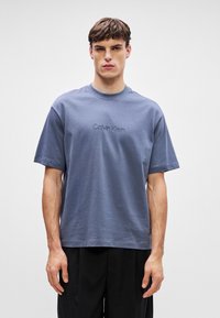 Majica kratkih rukava, okruglog izreza, plave boje od pamuka s vezom "Calvin Klein" na sredini. Glatka tekstura, opušten fit.