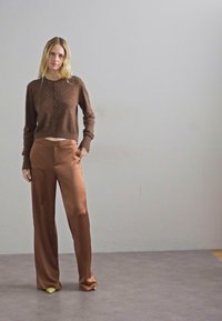 Καφέ, υφασμάτινο πλεκτό ζακετάκι με cropped σχέδιο και κλείσιμο με κουμπί, συνδυασμένο με ψηλόμεσο, ρέων καφέ σατέν παντελόνι.