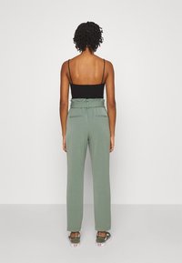 Pantalons verts taille haute avec une coupe décontractée, dotés de deux poches arrière et d'une taille froncée. Portés avec un débardeur noir simple.