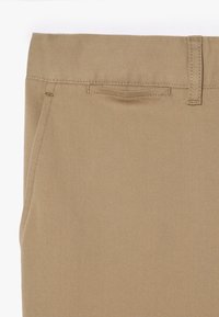 Calças de algodão bege com textura suave, trama diagonal, passantes para cinto e um discreto bolso lateral. Design ajustado com perna straight.
