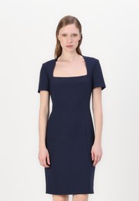 Mornarji modra obleka s kratkimi rokavi, kvadratnim izrezom in strukturiranim trupom. Gladek material z čistimi linijami in minimalnimi detajli.