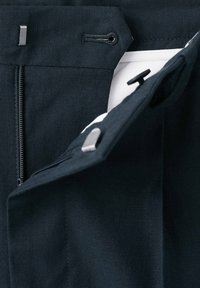 Gros plan de la fermeture d’un pantalon noir montrant la fermeture éclair, le bouton, le crochet et la boutonnière sur la ceinture en tissu.