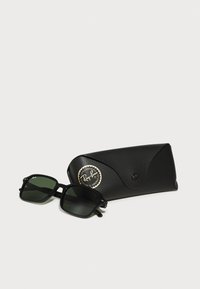 Mustat Ray-Ban aurinkolasit vihreillä linsseillä ja neliömäisellä muodolla. Mukana musta teksturoitu nahkakotelo, jossa on kultainen logo.