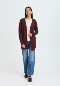 Cardigan in magenta a maglia con apertura frontale, maniche lunghe e polsini a costine, indossato sopra un top chiaro e abbinato a jeans a gamba larga.