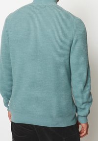 Pull bleu clair côtelé avec manches longues et col montant. La texture est tricotée, offrant une finition douce avec un ourlet ajusté.