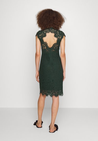 Πράσινο φόρεμα από δαντέλα με καπέλες μανικιών, ανοιχτή πλάτη και οδοντωτό στρίφωμα. Κοντή γραμμή που αναδεικνύει το περίπλοκο σχέδιο και την υφή της δαντέλας.