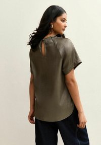 Top corto de color verde oliva, con mangas cortas y textura acanalada, que presenta un escote redondo y un pequeño detalle de ojal en la espalda. Combinado con jeans oscuros.