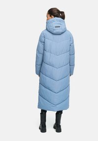 Cappotto lungo imbottito di colore azzurro chiaro con motivo a zig-zag, cappuccio staccabile e polsini a coste, abbinato a stivali neri fino al ginocchio.