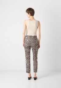 Haut sans manches beige associé à un pantalon blanc ajusté portant un imprimé léopard marron, silhouette slim, et des sandales à talons carrés noires.