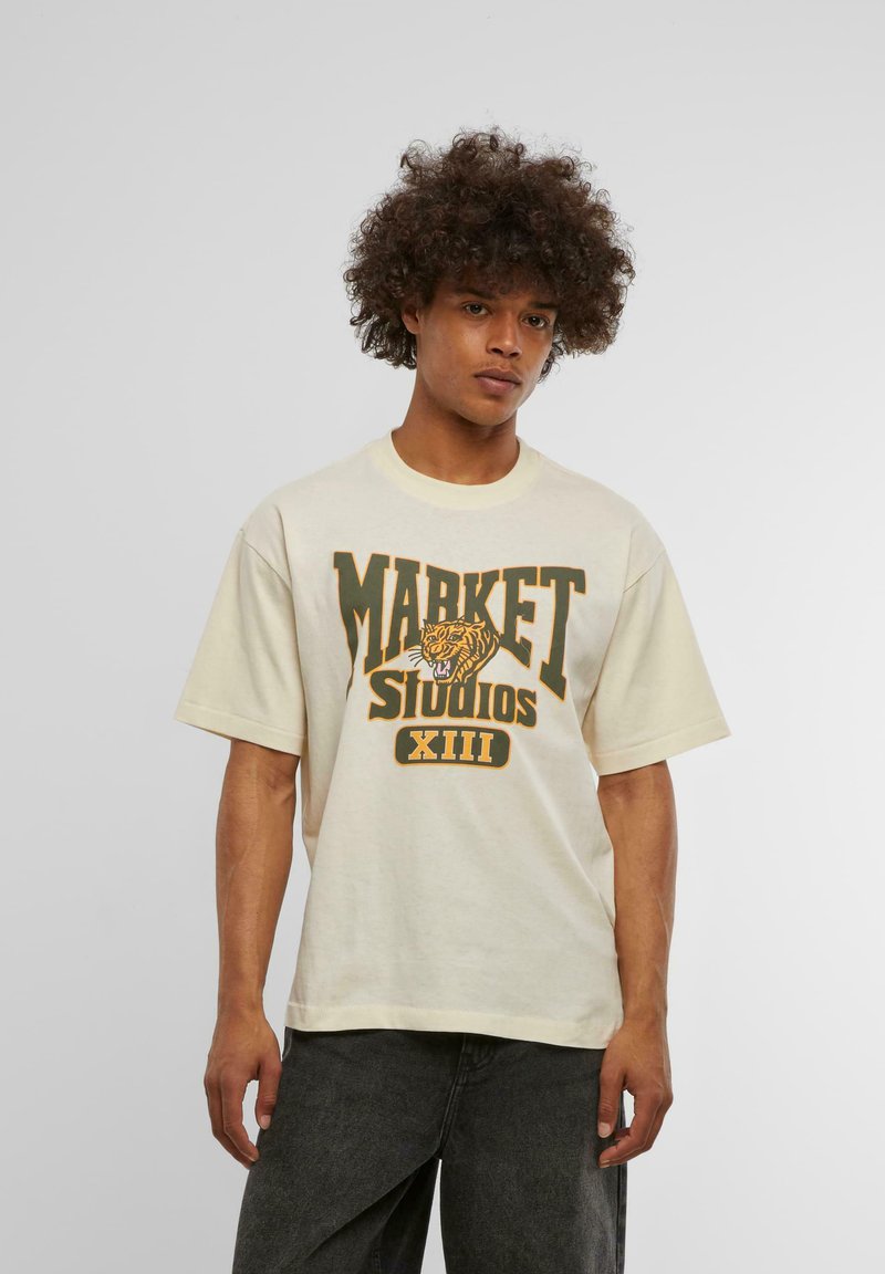 Krémové oversized tričko s grafikou v zelené a žluté barvě, na které je nápis "MARKET STUDIOS" a tygr, krátké rukávy a žebrovaný kulatý výstřih.