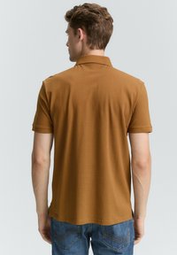 Brun polo t-shirt med korte ærmer, lavet af glat stof. Har en klassisk krave og en skræddersyet pasform, parret med blå jeans.
